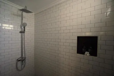 a white tiled bathroom with a shower with two bottles at Oemah Djoglo Kerobokan in Kerobokan
