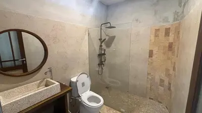 a bathroom with a toilet and a shower and a mirror at The Kutata in Jimbaran