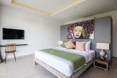 a bedroom with a large bed with a painting on the wall at Villa Elisa in Canggu
