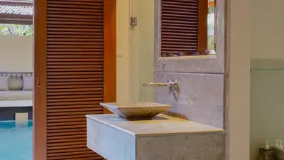 a bathroom with a stone sink next to a pool at Jepun Villa by Betterplace in Seminyak