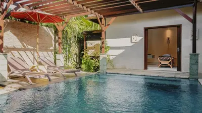 a pool with chairs and an umbrella next to a house at Jepun Villa by Betterplace in Seminyak