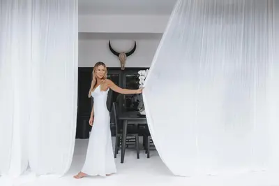 a woman in a white dress standing behind a curtain at Villa Manis Kecil in Seminyak