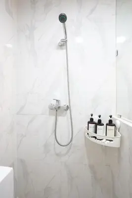 a white bathroom with a shower with three bottles on a shelf at Mezzanine Luxury Smart Room - Sanur in Sanur