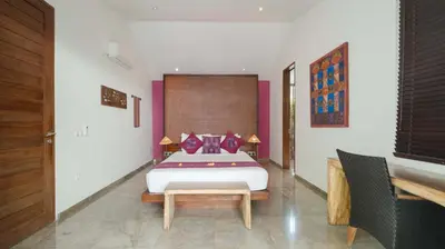 a bedroom with a king sized bed and a table at Villa Anjali Purple by Villa Finder in Seminyak