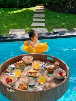 a child in a raft in a pool with a table of food at Villa Taman Rahasia, Sitara Villa Group in Seminyak