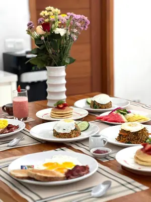 a table with plates of food and a vase of flowers at Villa Taman Rahasia, Sitara Villa Group in Seminyak