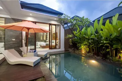a swimming pool with an umbrella and a chair at Puri Sahadewa Seminyak in Seminyak