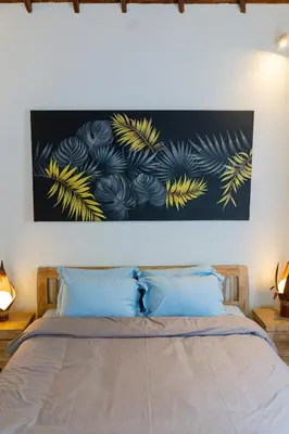 a painting hangs above a bed with blue pillows at Peaceful 2br with pool & garden in Seminyak