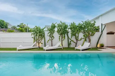 a pool with trees and lounge chairs next to a building at Villa Wuizy By DreamAwayBali in Seminyak