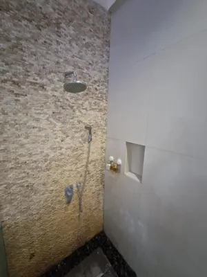 a shower in a bathroom with a stone wall at Max Guest House in Seminyak