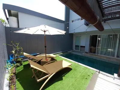a patio with chairs and an umbrella next to a swimming pool at PalmA Private Villa - A Leafy Place in Mumbul Hill in Nusa Dua