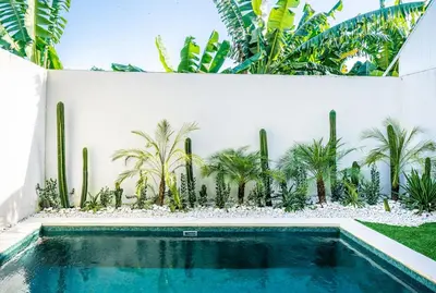 a swimming pool with palm trees and a white wall at Renjana Villa-2BR Modern Tropical Villa in Seminyak with Private Pool & Rice Field View in Seminyak