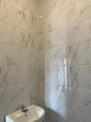 a white tiled bathroom with a toilet and a sink at Kubu Gandi Homestay in Denpasar