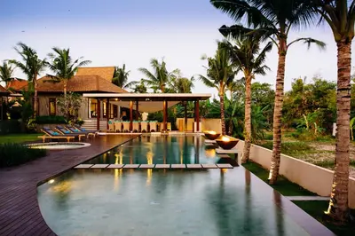 a swimming pool in front of a house with palm trees at Umah Daun by Nakula in Canggu