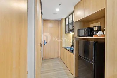 a kitchen with wooden cabinets and a black refrigerator at Rivana by Kozystay - Nusa Dua in Nusa Dua