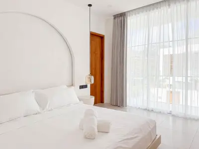 a white bedroom with a white bed and a large window at Anjou - Twin Villa in Berawa Canggu in Canggu