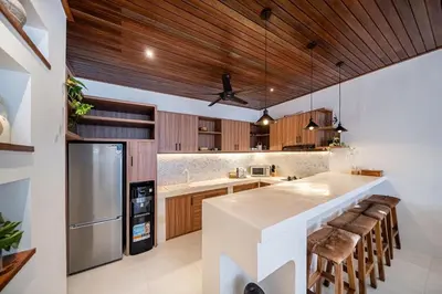 a kitchen with wooden ceilings and a large island with bar stools at Villa Mai Mai Seminyak in Seminyak