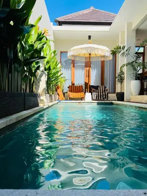 a pool in front of a house with an umbrella at Villa Karma Damai in Seminyak