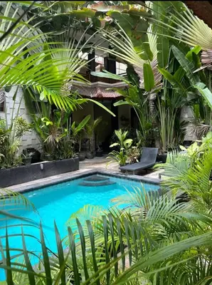 a swimming pool in a garden with palm trees at Cempaka Apartment Surfaris Inn in Legian