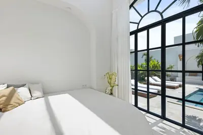 a white bedroom with a bed and a large window at All-White Villa with Pool, Sauna, Firepit & Office in Jimbaran