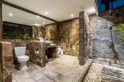 a stone bathroom with a toilet and a sink at The Hijau Damai Villa in Seminyak
