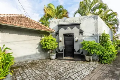 a white house with a black door and trees at The Hijau Damai Villa in Seminyak
