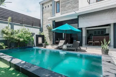 a swimming pool with an umbrella next to a house at Villa Nakula - Managed By Chayah Bali Villa Group in Seminyak