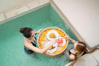 two women holding a tray of food in a swimming pool at Villa Azura in Perean