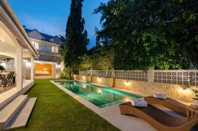 a swimming pool in a yard with two benches and a house at The Heritage 4BR Villa Luxury Oasis in Canggu