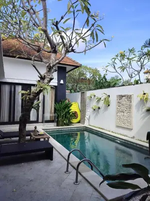 a man sitting next to a swimming pool next to a house at Villa LYM BALI 3br with private pool in Legian