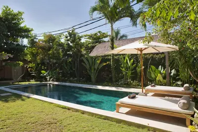 a swimming pool with an umbrella and a bench at Two bedroom Villa in a beautyful tropical garden in Seminyak