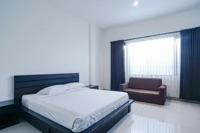 a bedroom with a bed and a chair and a window at Prima Inn in Kuta