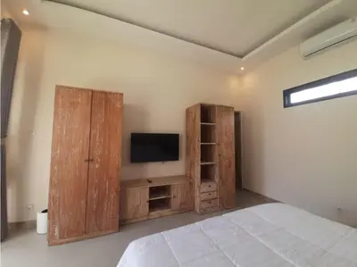 a bedroom with a bed and a tv and wooden cabinets at Villa Rova in Kerobokan