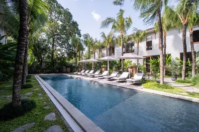 a swimming pool with lounge chairs and palm trees at Anam Tang New Rooms & Cafe near Seminyak in Seminyak