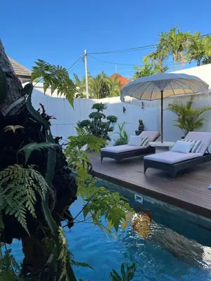 a resort with a pool with two beds and an umbrella at Deo Villa Seminyak in Seminyak