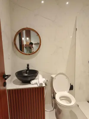 a man taking a picture of a bathroom with a toilet at Apartemen JIRO BALI in Ngurah Rai International Airport