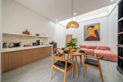 a kitchen and living room with a table and a pink couch at Kutesa Villa - Cozy Villa with Dreamy Swim Spot in Kerobokan