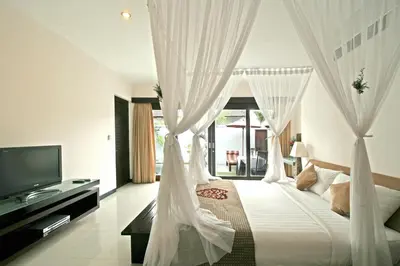 a bedroom with a bed with white curtains and a television at Rishi Villas in Kerobokan