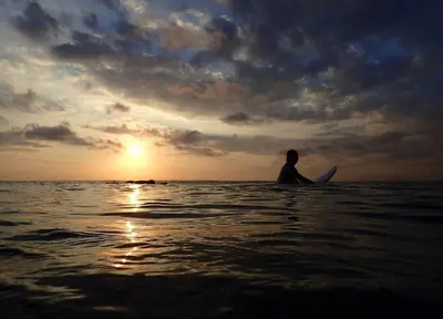 a person sitting on a surfboard in the ocean at SG Hotel - 2 Minutes to the Beach By Micky Studio 2 in Legian
