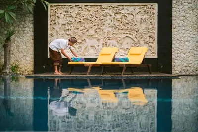 a man standing next to two chairs next to a swimming pool at The Casa Amaya By Puri Asia in Jimbaran