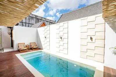 an outdoor swimming pool with two chairs next to a building at Villa Tirtha at Nara Villa in Seminyak