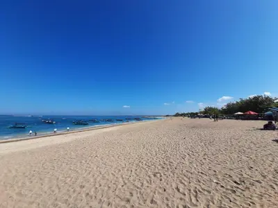 a sandy beach with people in the ocean on a clear day at ABI Hotel2 - 1 minute to the Beach and 1 second to the Mall in Ngurah Rai International Airport