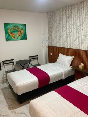 a bedroom with two beds and a table at Hotel Sanrina Kuta Bali in Kuta