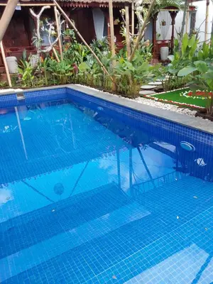 a large swimming pool with blue tiles in a yard at Navalia Rumah Kayu in Kerobokan