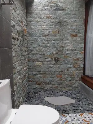 a bathroom with a white toilet and a stone wall at Navalia Rumah Kayu in Kerobokan