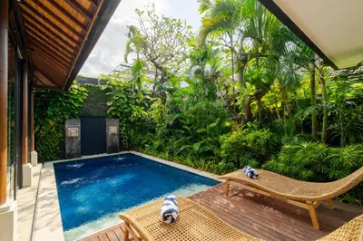 a swimming pool in a garden with a chair and a table at Boholuma Villas by Pertama Management in Seminyak