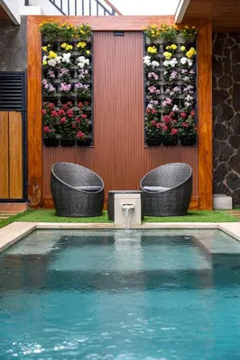 a swimming pool with two chairs and flowers on a wall at The Saren CoLiving by SooBali in Kerobokan