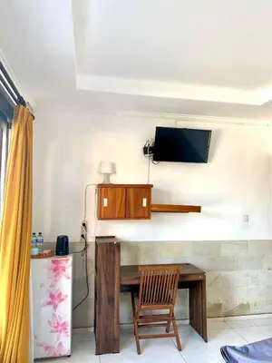 a room with a table and a television on a wall at Karna Guest House in Seminyak