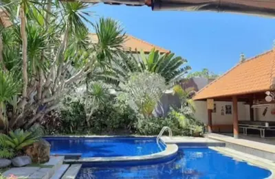 a swimming pool in front of a house with palm trees at Sandy Shores Bali in Seminyak