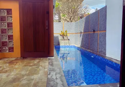 a swimming pool next to a house with a red door at Villa Casanomi By Pandara in Kerobokan